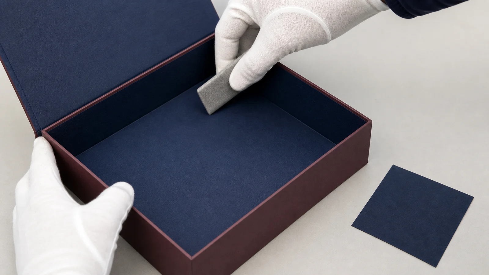 Finished navy inner lining being smoothed into the corner of an open rigid gift box